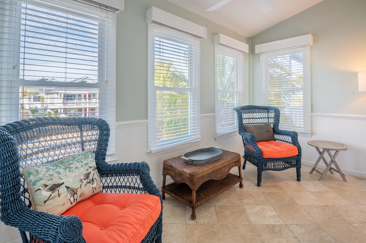 A cozy seating area with blue wicker chairs and orange cushions sits around a wooden coffee table, with textured pillow accents. The relaxed mood and morning light hint at a perfect spot to review the day's adventures or enjoy a quiet break between outings.