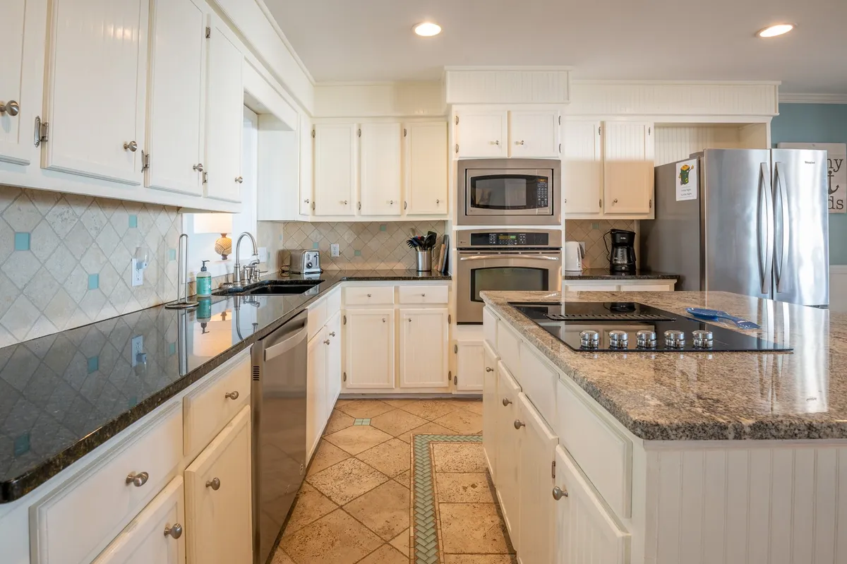A spacious, open-concept kitchen featuring granite countertops, stainless steel appliances, white cabinetry, and a large island, with plenty of room for meal prep and socializing. The setup is ideal for group cooking and family gatherings, with a warm and welcoming atmosphere.