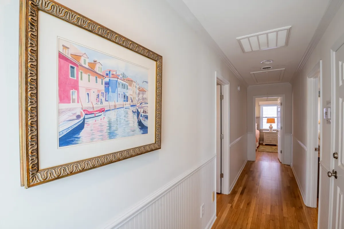 A cheerful hallway featuring a vibrant painting of a waterfront scene, warm wooden flooring, and multiple doorways leading to other spaces. The painting evokes the lively coastal atmosphere and the promise of outdoor adventure, while the hall itself feels welcoming and open.