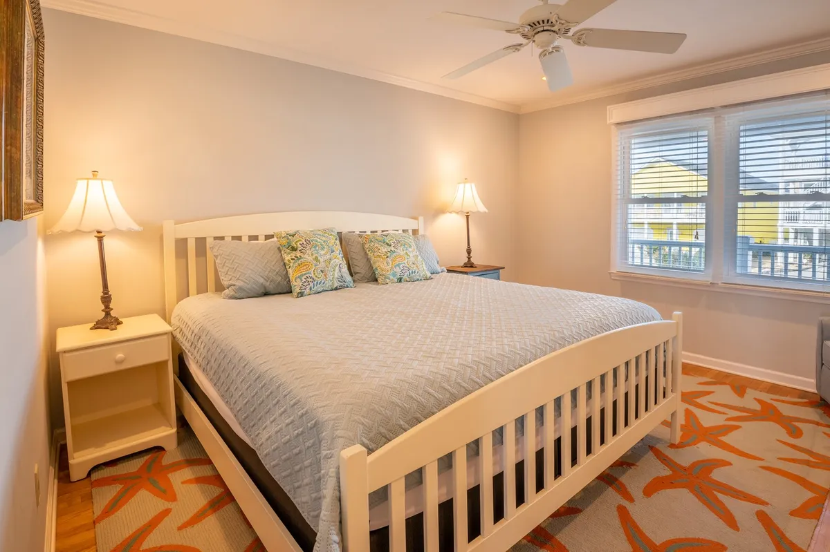 This image captures a calm and cozy bedroom featuring a comfortable bed, warm lighting from bedside lamps, a soft rug, and windows that invite natural light. The tranquil ambiance is perfect for rest and relaxation, aligning with the section’s emphasis on restful sanctuaries and plush bedding.