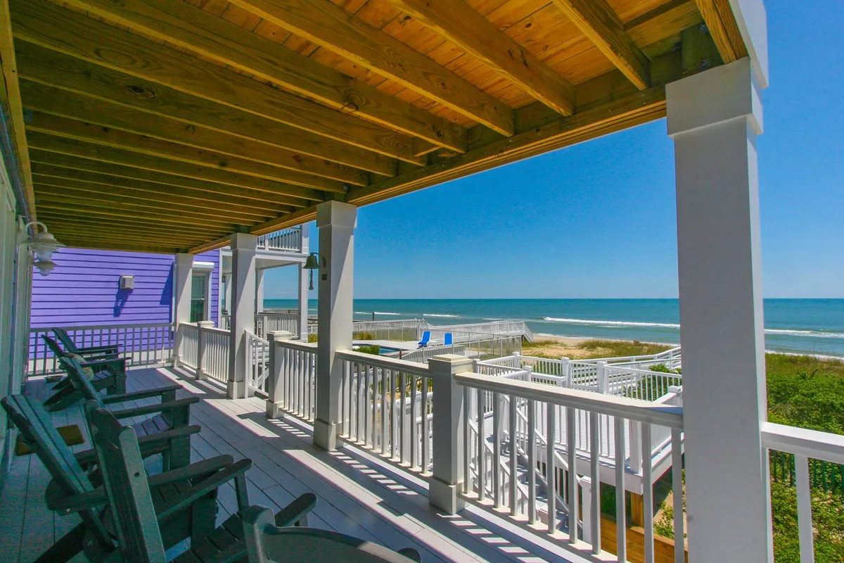 This tranquil exterior shot features deck chairs and white railings, with a stunning ocean view and the distinctive purple house facade. The inviting seating area is oriented toward the water, encouraging guests to spot dolphins or enjoy gentle sea breezes.