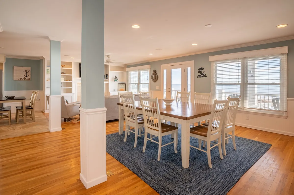 A spacious, light-filled dining area is showcased with a large dining table, an open concept layout, generous windows offering views outside, and a blue accent wall. The space feels inviting and ideal for both formal dinners and casual breakfasts.