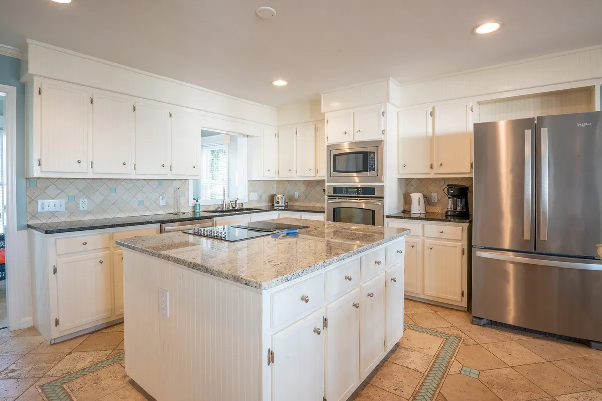 This image depicts a fully equipped kitchen featuring a stunning granite island, stainless steel appliances, and ample counter space. The central island is the visual and functional heart of the space, inviting cooking, baking, and socializing.